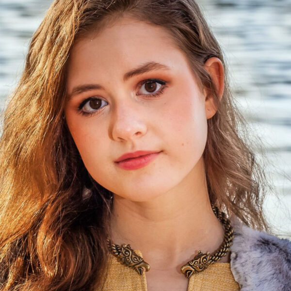 A young girl in a fur coat posing by the water showcases her Celtic-inspired fashion, accentuated by a beautiful Celtic Griffin Neck Torc.