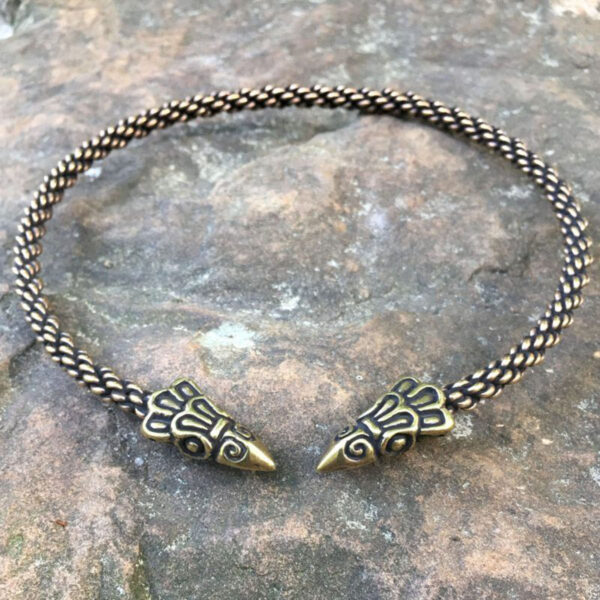 A gold and black Celtic Raven Neck Torc delicately braided into a choker, resting gracefully on a rock.