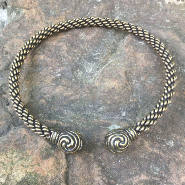 A Celtic Triskelion Neck Torc braided bracelet on a rock.