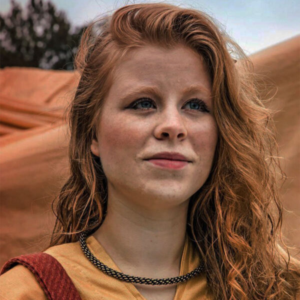 A young woman with red hair standing in front of a tent, wearing The Viking Neck Torc.