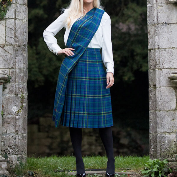 A woman in a Welsh Tartan Medium Weight Premium Wool Fiona Kilted Skirt posing in front of a stone wall.