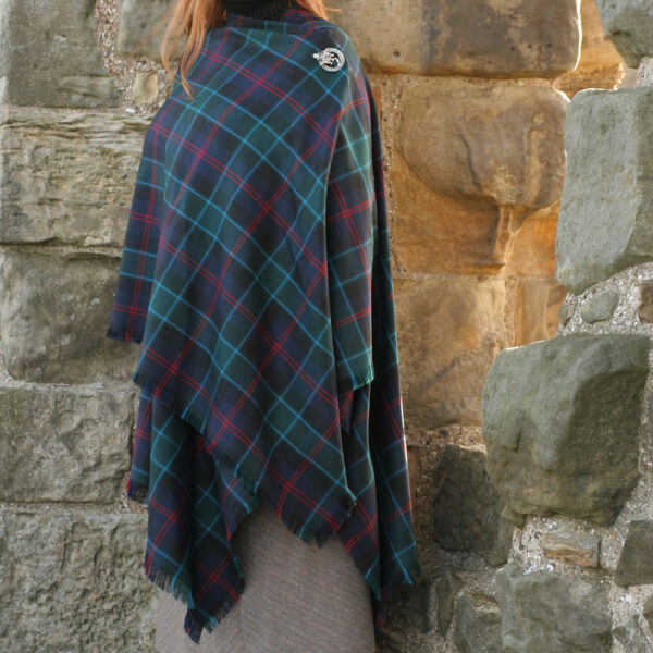 An Irish woman wearing an Irish County Tartan Serape - Spring Weight Premium Wool in front of a stone wall on a spring day.