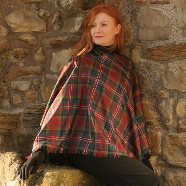 A red haired woman wearing a tartan poncho, accessorized with the Spring Weight Tartan Shawl.