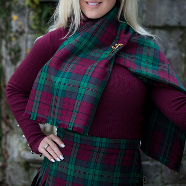 A woman in a red and green plaid kilt posing for a picture, wearing a Welsh Tartan Shawl, Medium Weight Premium Wool.