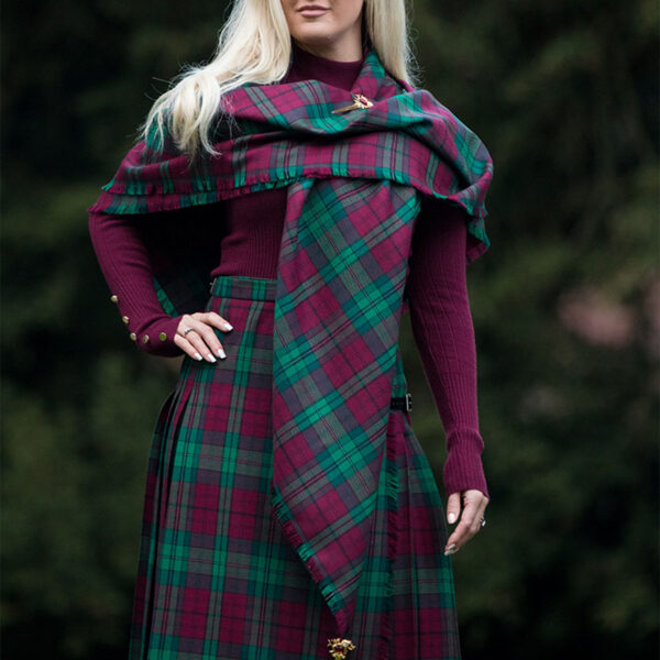 A woman in a plaid kilt posing for a picture with a Welsh Tartan Shawl, Medium Weight Premium Wool draped elegantly over her shoulders.