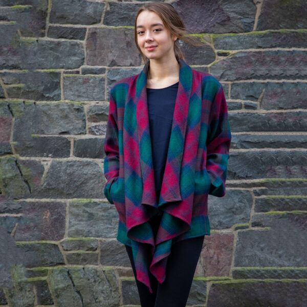 A woman wearing a Scottish Lambswool Tartan Kerry Jacket standing in front of a stone wall.