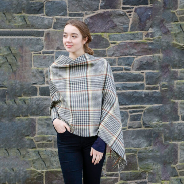 A woman wearing a Scottish Lambswool Tartan Poncho standing in front of a stone wall.
