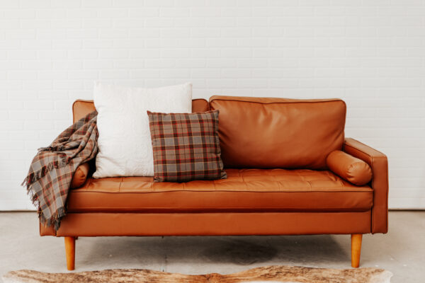 A brown leather couch with OUTLANDER Throw Pillow Cover Authentic Premium Wool Tartan throw pillows and a sheepskin rug.