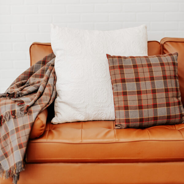 A couch with OUTLANDER Throw Pillow Cover Authentic Premium Wool Tartan and a blanket.