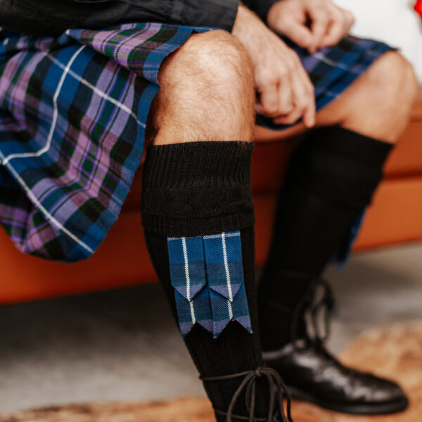 A man in a plaid kilt sitting on a couch.