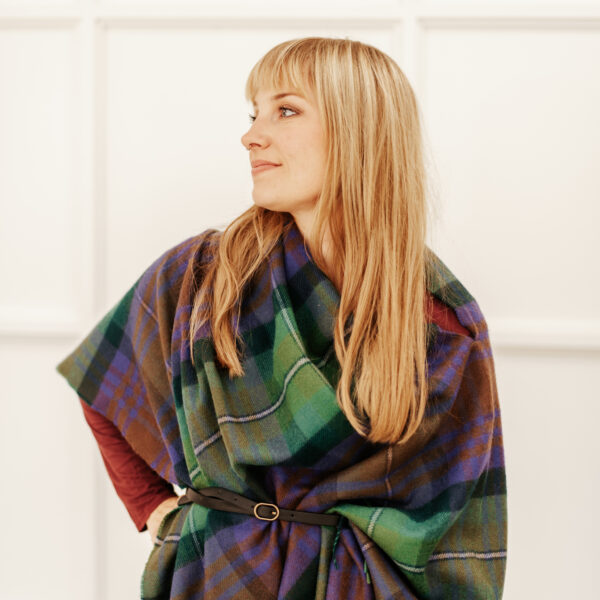A woman wearing a Scottish Lambswool Tartan Poncho standing in front of a white wall.
