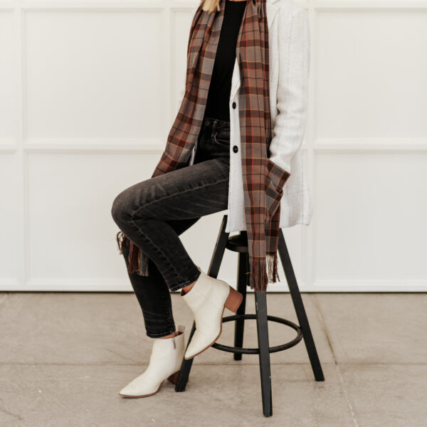A woman sitting on a stool wearing a Tartan Pocket Scarf - Homespun Wool Blend.