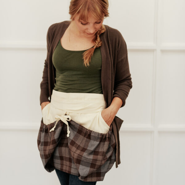 A woman wearing a plaid apron with pockets.