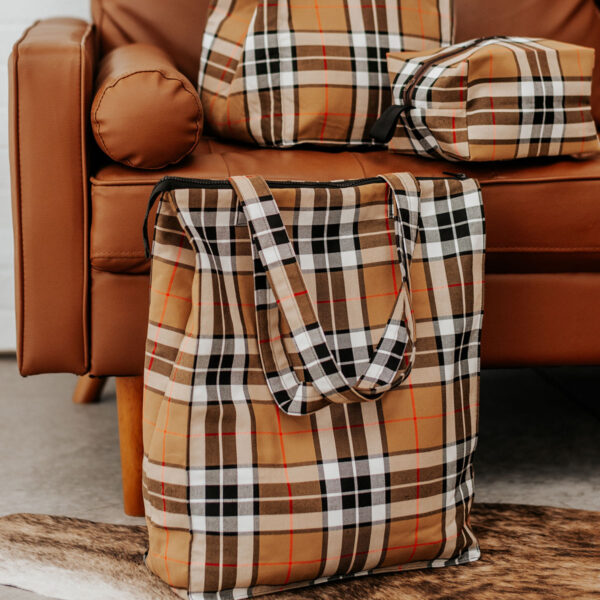 A NLA Jenny tartan travel bag with a brown plaid pattern, constructed from poly/viscose wool-free fabric, perfectly complements a cozy brown couch.