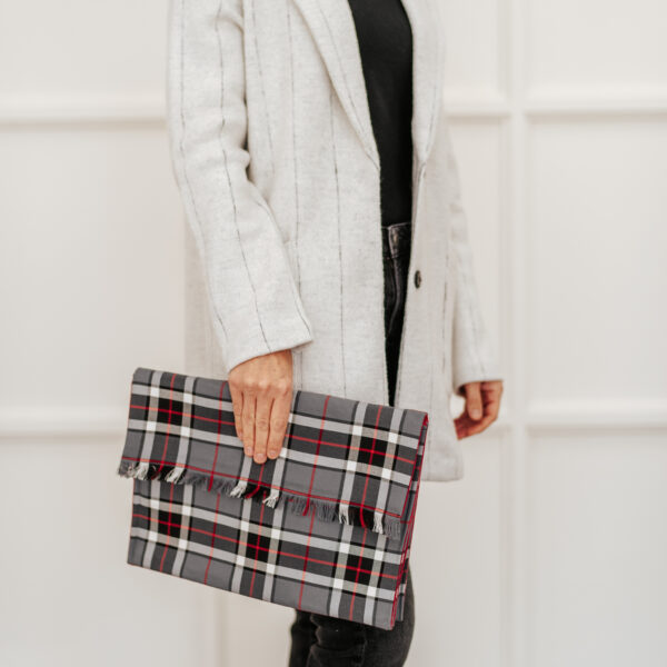 A woman stylishly accessorized with a Tartan Folio - Poly/Viscose Wool Free, a plaid clutch bag made of poly/viscose wool-free fabric.