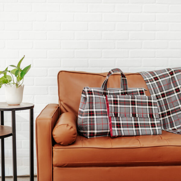 A Tartan Purse - Poly/Viscose Wool Free sits on a brown couch next to a potted plant.
