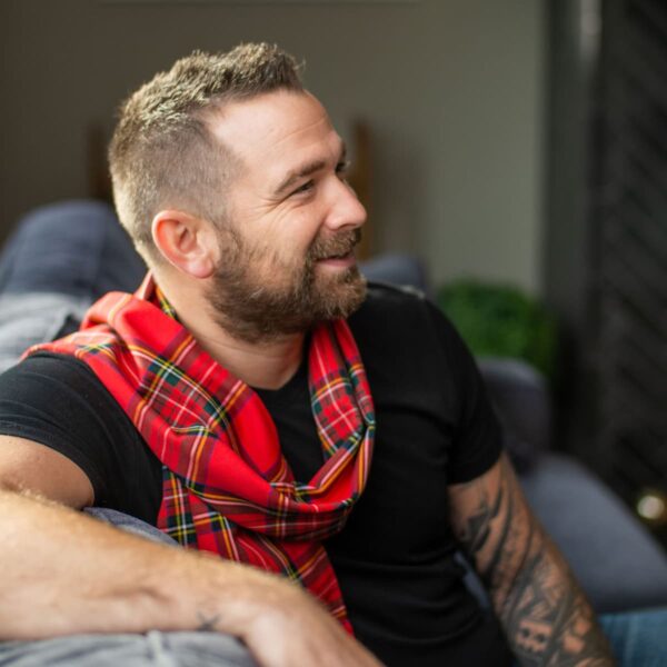 A man sitting on a couch wearing a red tartan scarf.
