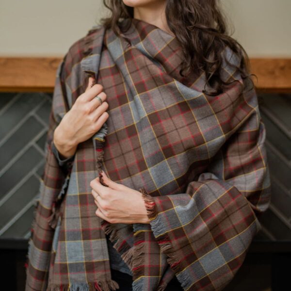 A woman wearing a plaid scarf in front of a fireplace.