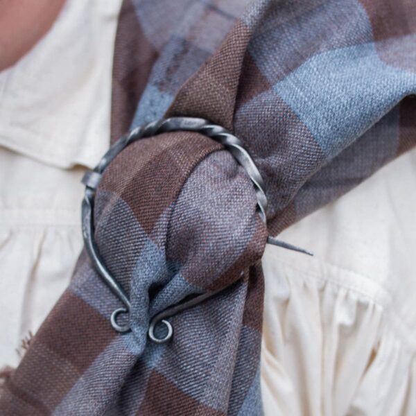 A man wearing a plaid scarf with a metal ring on it.
