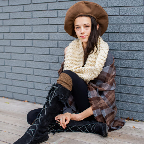A woman wearing a hat and boots sitting on a sidewalk.