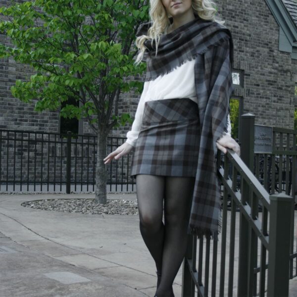 A woman in a plaid skirt posing on a railing, wearing an OUTLANDER Billie-Style Kilted Mini-Skirt Poly/Viscose made of poly/viscose fabric.