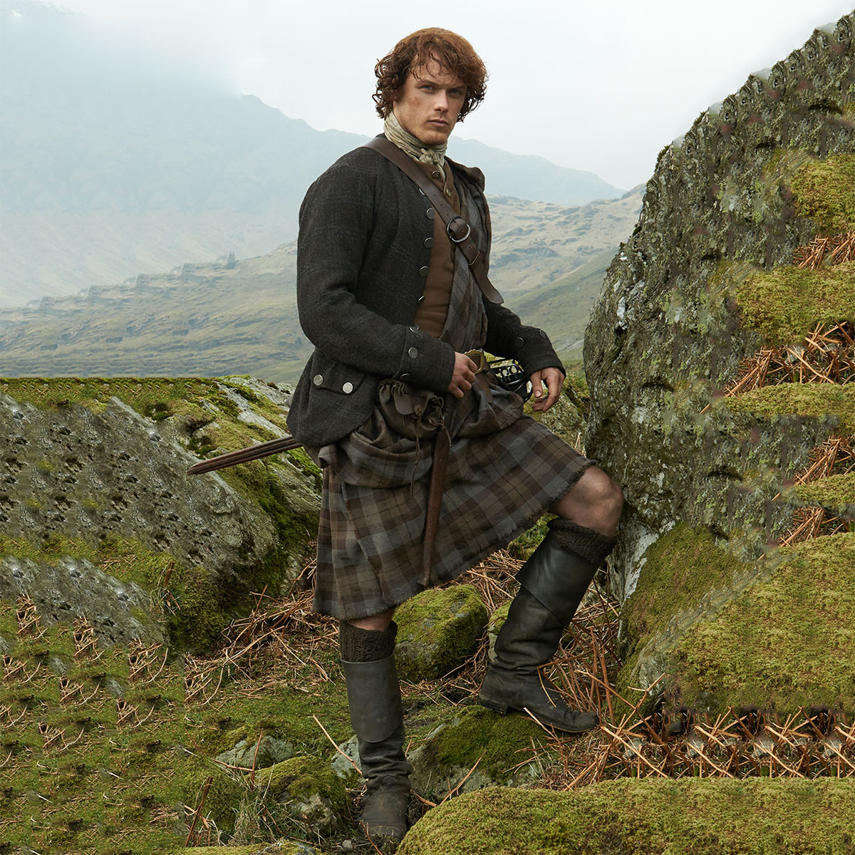 A man in a kilt standing on a grassy hill.