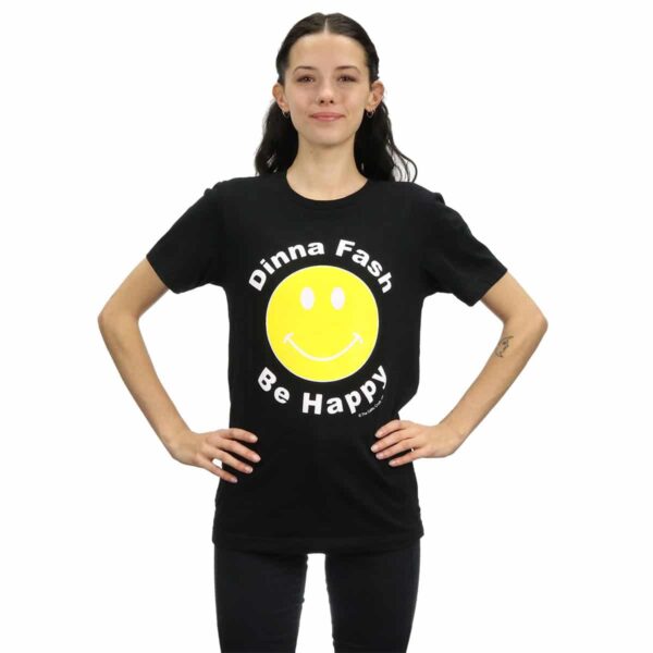 A woman wearing a black Dinna Fash - Be Happy T-Shirt with a smiley face on it.