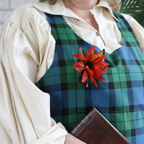 A woman wearing a Tartan Cross Back Apron - Homespun Wool Blend with a flower in her hair.
