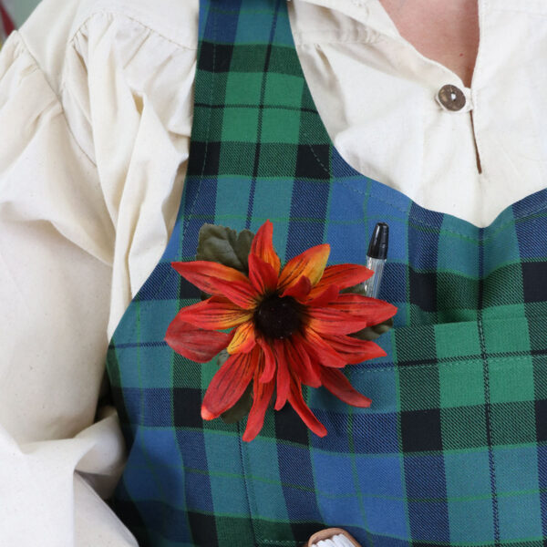 A woman wearing a Tartan Cross Back Apron - Homespun Wool Blend with a flower on it.