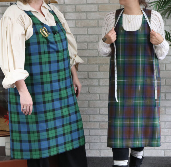 Two women standing next to each other wearing Tartan Cross Back Aprons made of a Homespun Wool Blend.