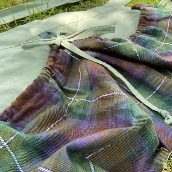 A Tartan Gathering Apron - Homespun Wool-Blend lying on the grass.