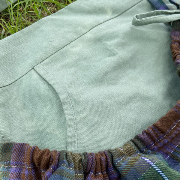 A close up of a Tartan Gathering Apron - Homespun Wool-Blend laying in the grass.