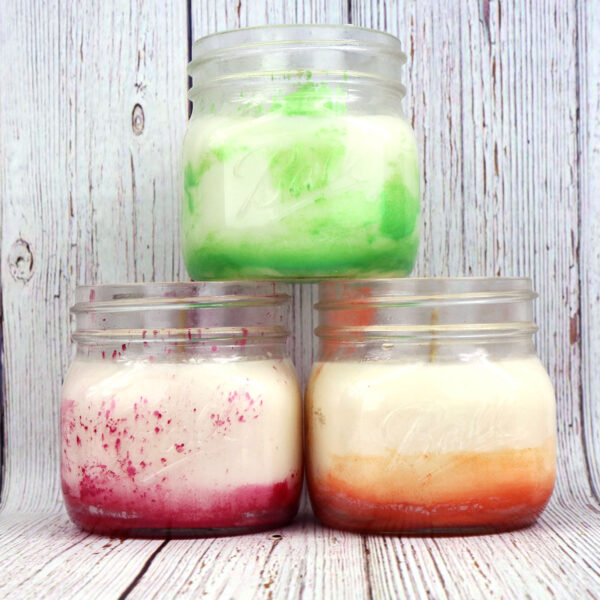 Homemade candles displayed in mason jars filled with vibrant colored liquids.