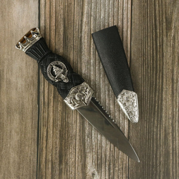 A knife with a leather sheath on a wooden table, adorned with Gaelic Themes Clan Crest Lapel Pin on the lapel.