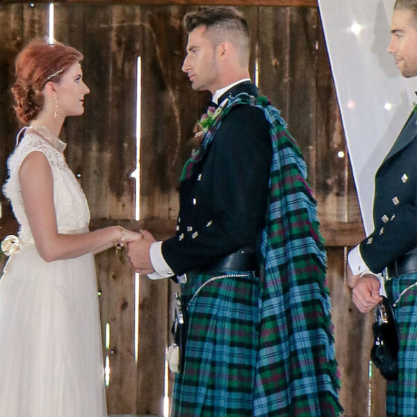 A bride and groom in kilts, adorned with a Homespun Wool Blend Tartan Fly Plaid, standing next to each other.