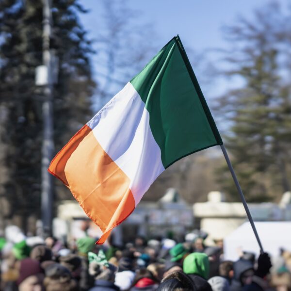 A crowd of people displaying their Irish spirit with an Irish flag waving in the air as part of their St. Patrick's Day outfit.