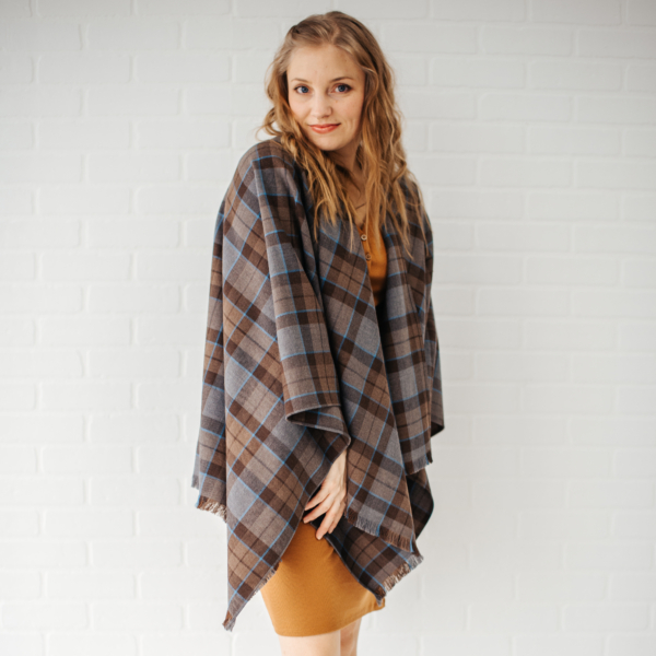 A woman wearing an OUTLANDER Wrap Premium Lambswool Tartan posing in front of a white wall.