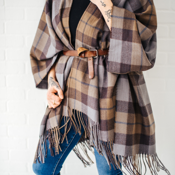 A woman wearing an OUTLANDER Wrap Premium Lambswool Tartan poncho and jeans.