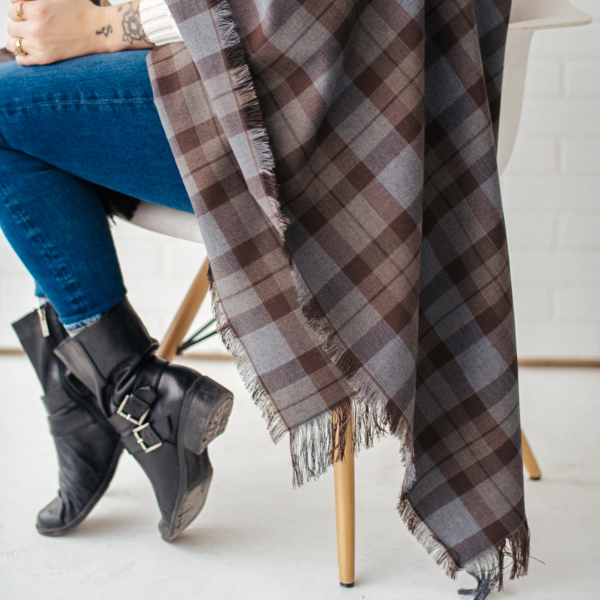 A woman sitting on a chair with an OUTLANDER Wrap Premium Lambswool Tartan.
