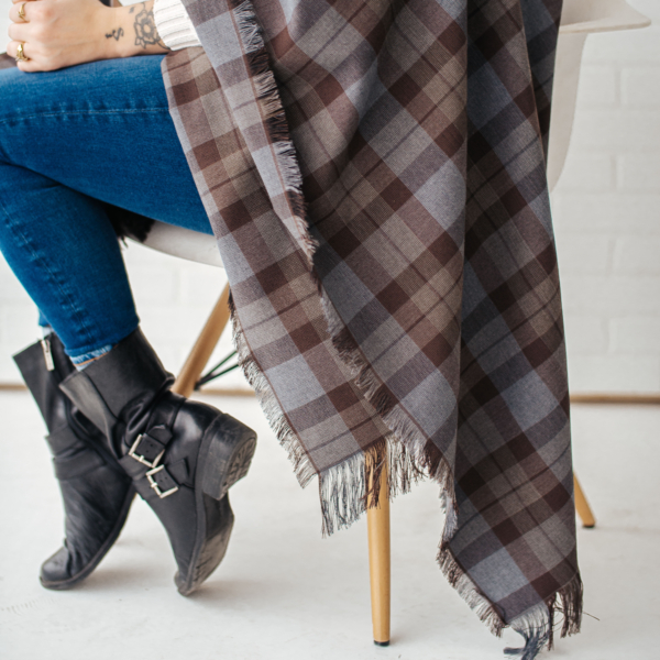 A woman, wrapped in an OUTLANDER Wrap Premium Lambswool Tartan, sitting on a chair.