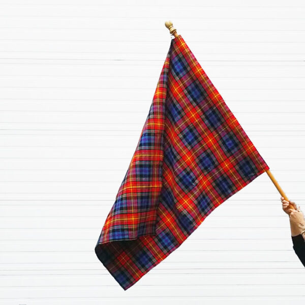 A person proudly waving a large LGBT Pride Tartan Flags - Homespun Wool Blend in front of a white wall.