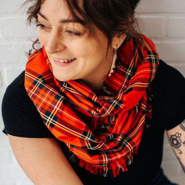 A woman with tattoos wearing a red tartan scarf.