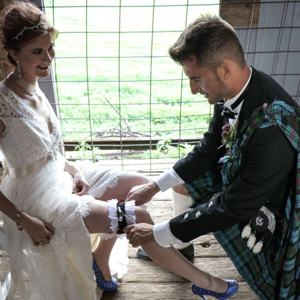 A bride and groom tying their Homespun Tartan Garter on a wooden floor.