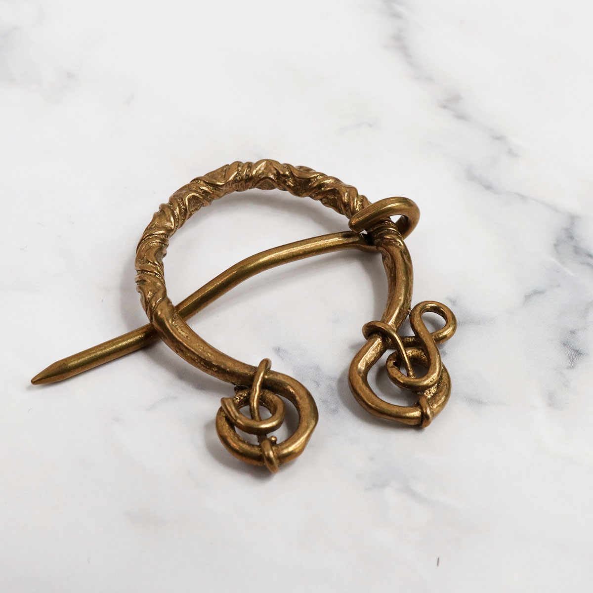 A pair of brass earrings on a marble table with an "Entangled Brass Penannular Brooch".