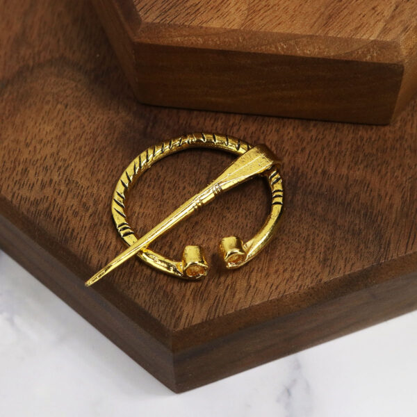 A mini Penannular Brooch on top of a wooden table.