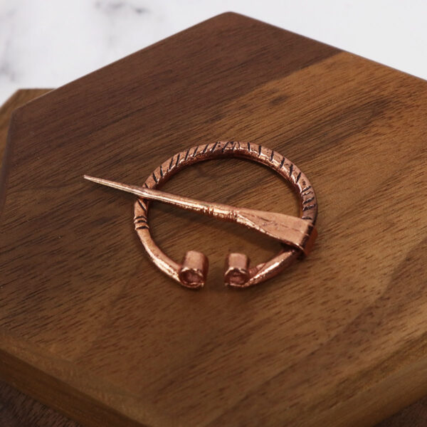 A Mini Penannular Brooch with a ring on top of a wooden box.