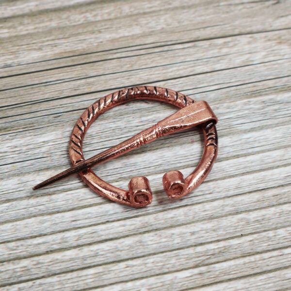 A miniature copper Mini Penannular Brooch on a wooden surface.
